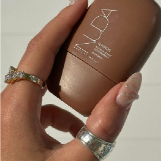 Hand holding a brown cosmetic product with 'Nuda' branding against a neutral background