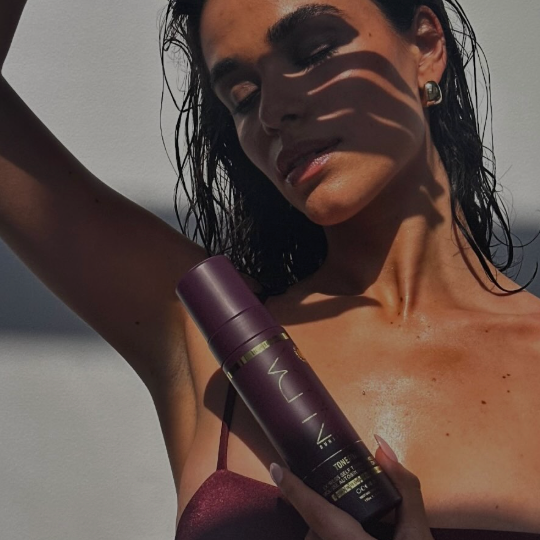 Woman holding a purple bottle with 'Nuxe' branding against a neutral background